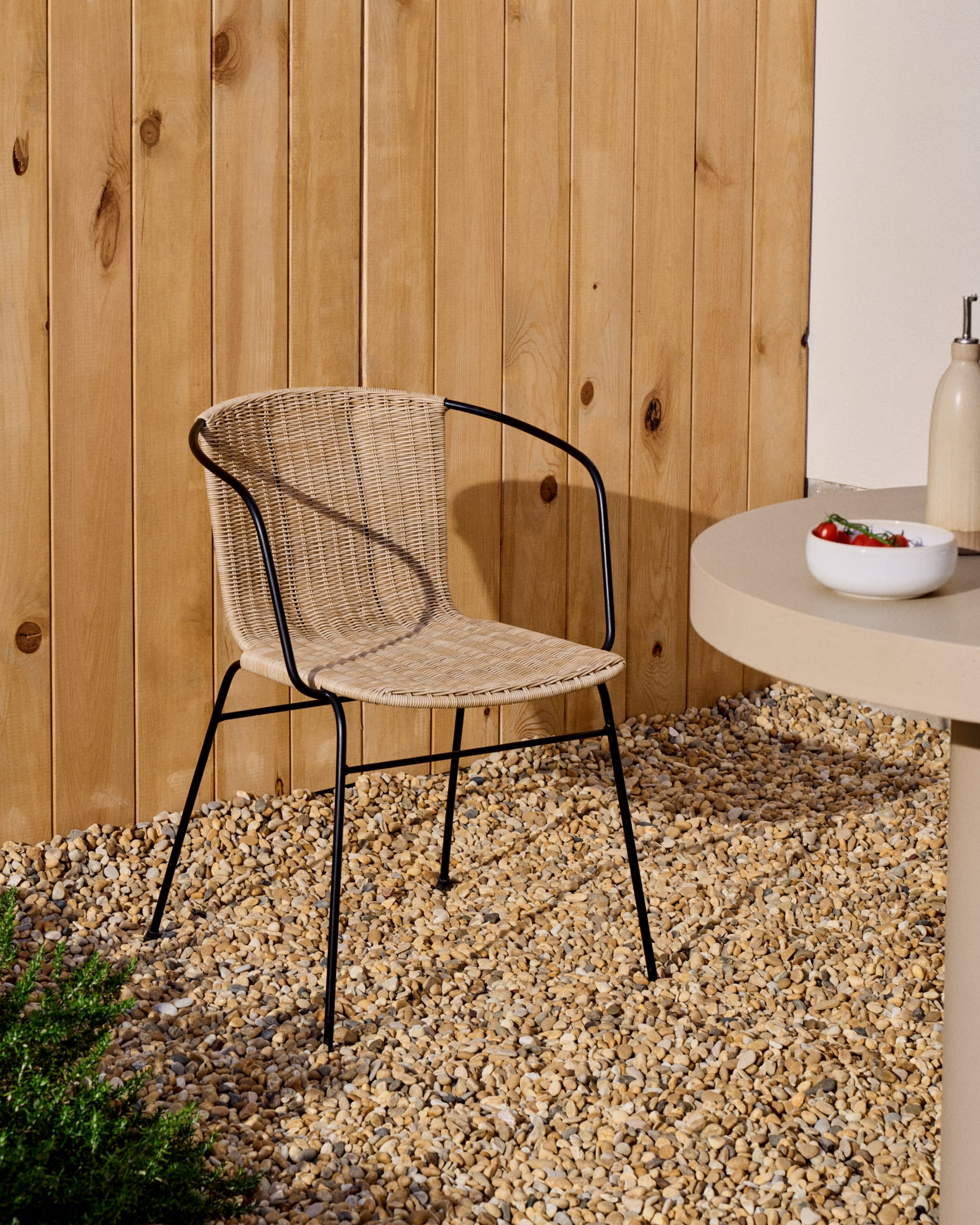 Eltiera stackable chair in synthetic rattan with black steel frame and armrests