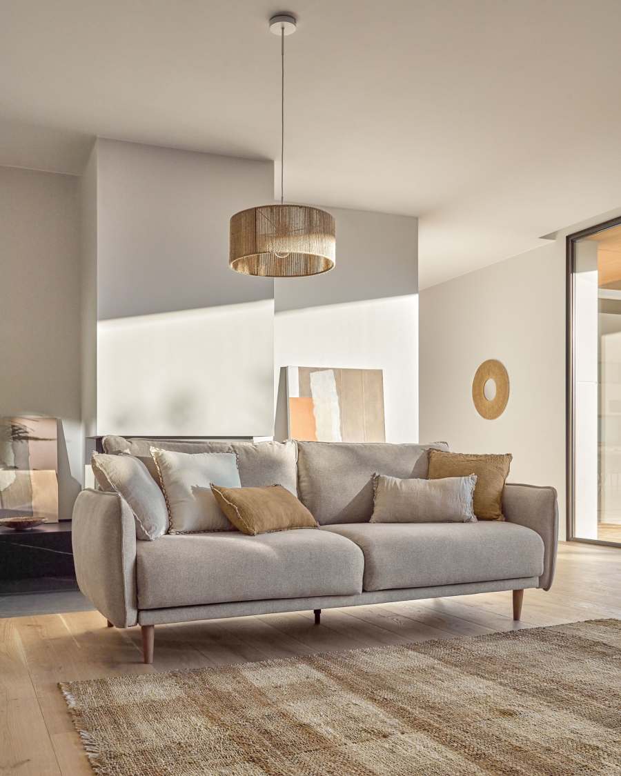 Canapé Carlota beige clair avec coussins ocre et crème dans un salon, suspension en osier.