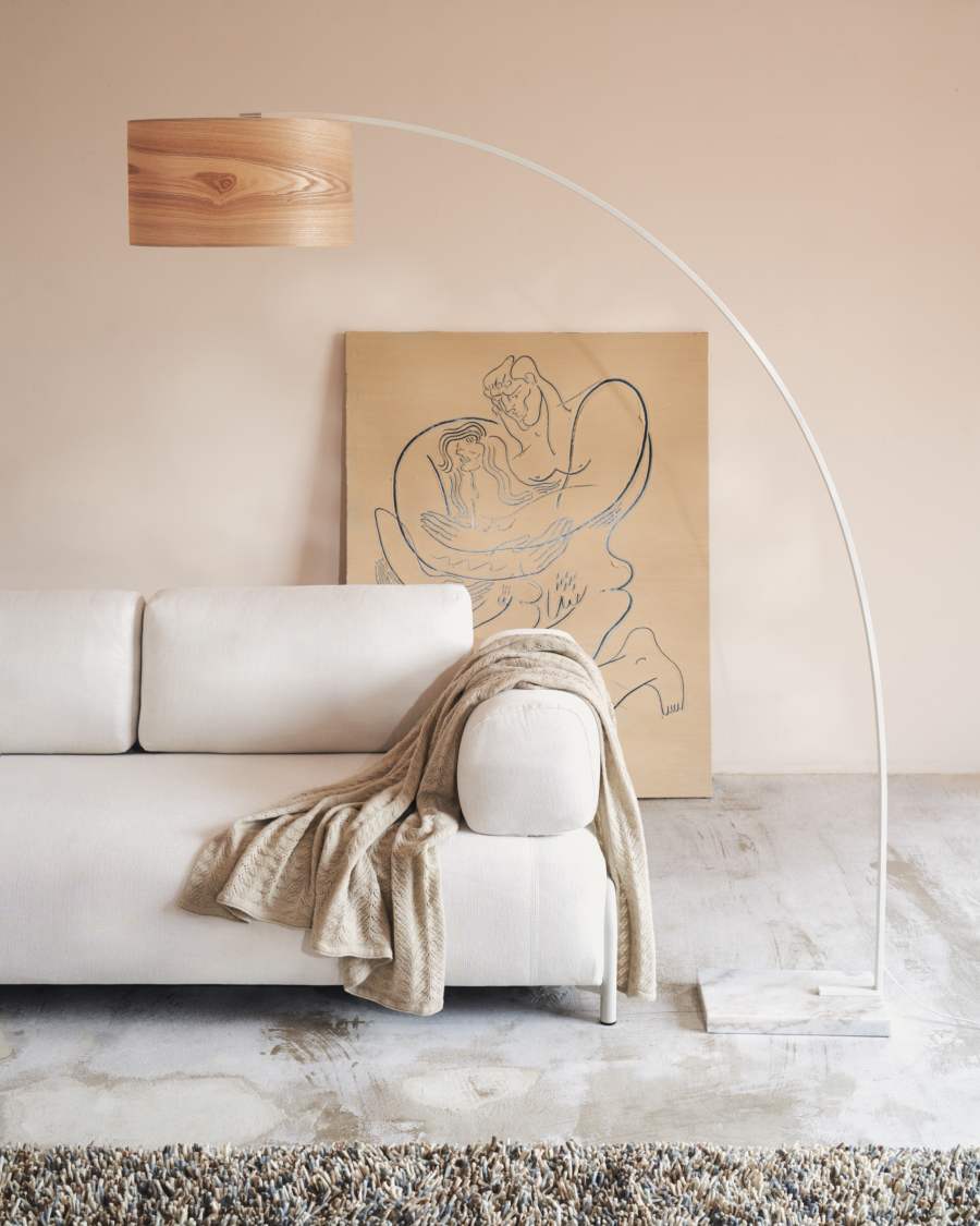 Canapé Compo blanc cassé couvert d'un plaid beige, près d'une lampe arquée blanche et d'un tableau.