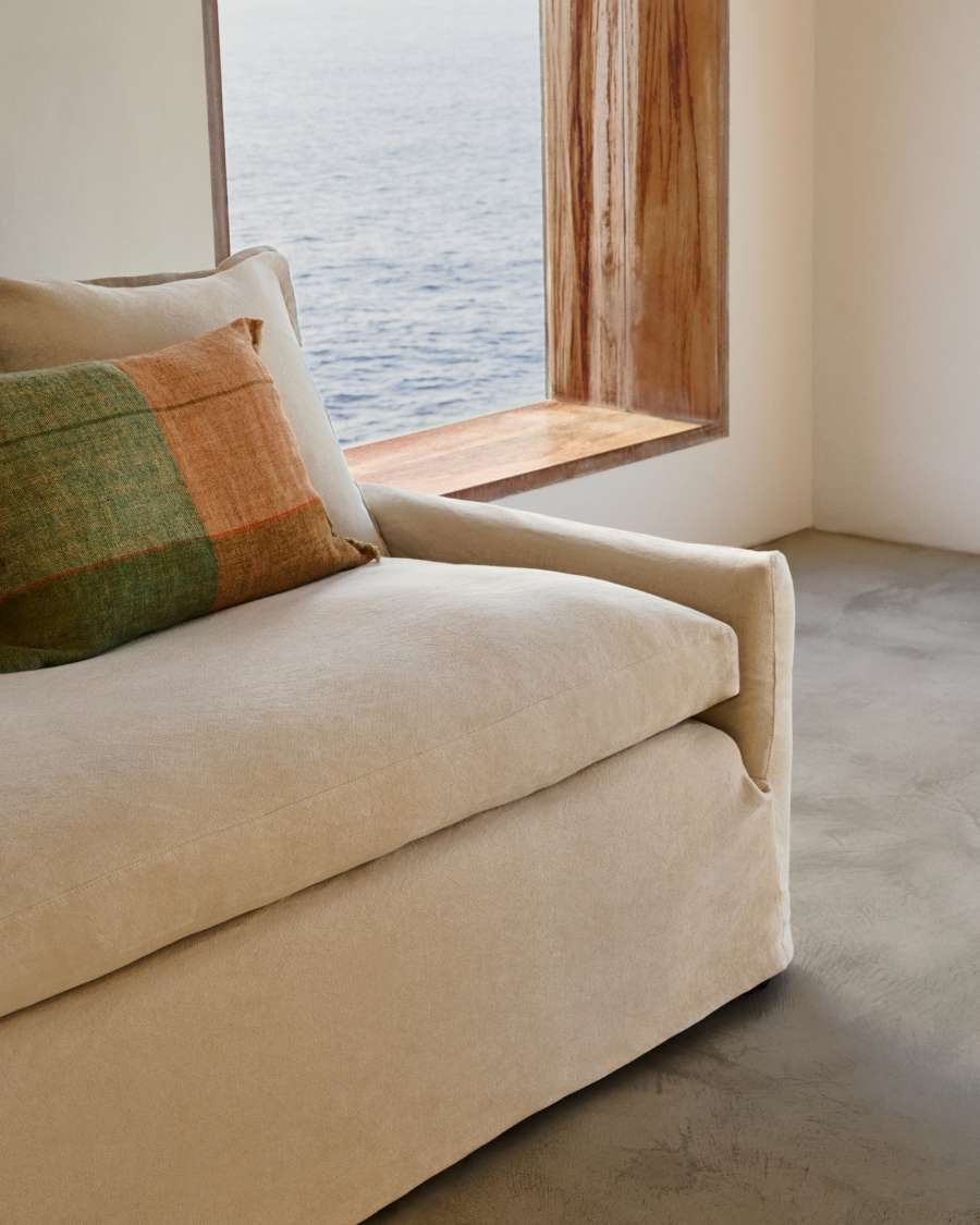 Gros plan de l’accoudoir et de l’assise du canapé beige, avec un coussin vert et orange.