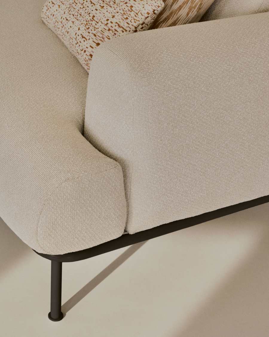Gros plan de l'accoudoir et du pied noir du canapé Aurum, avec un coussin au fond.