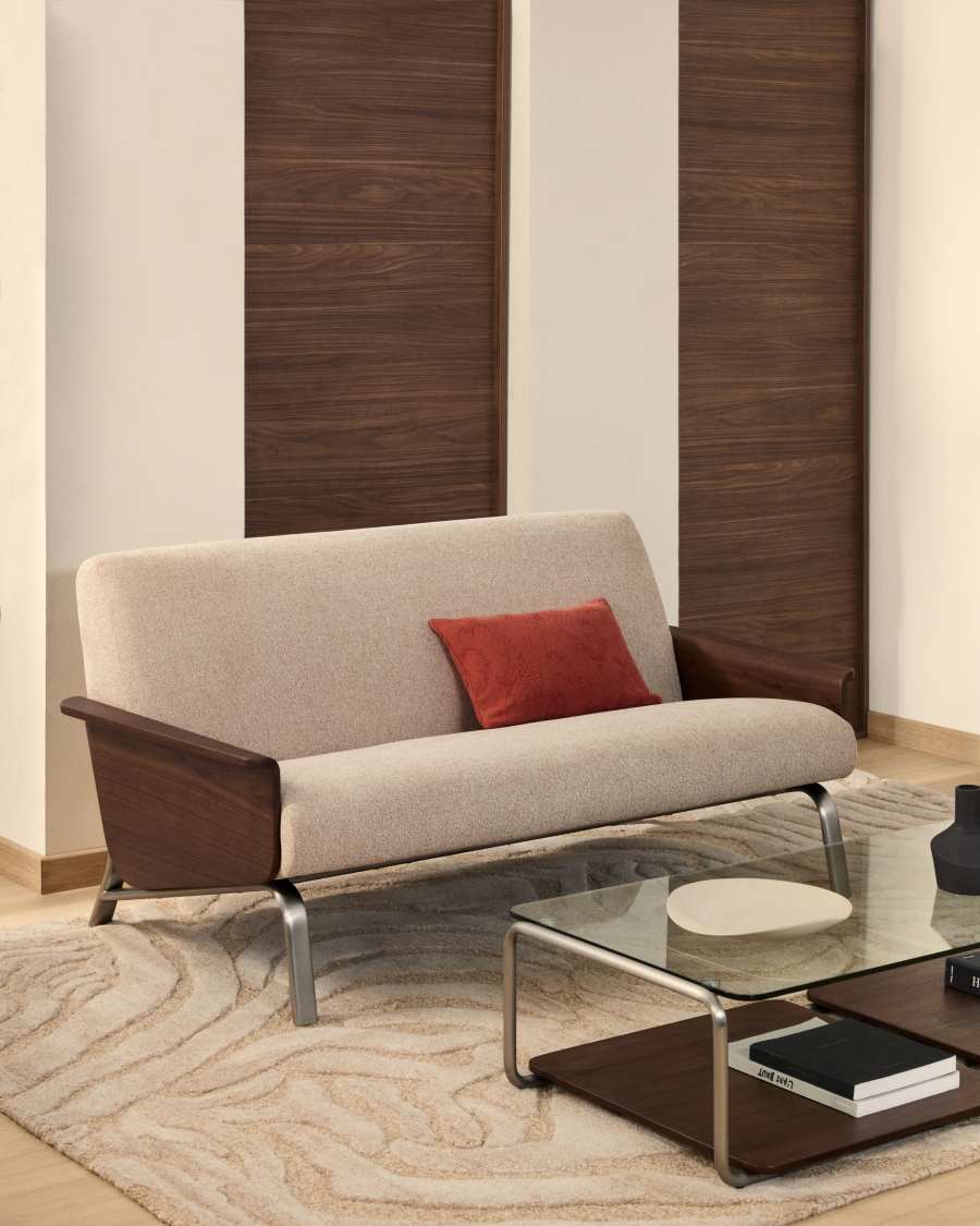 Canapé Amsen beige avec accoudoirs en noyer et coussin rouge, devant des panneaux de bois sombre.