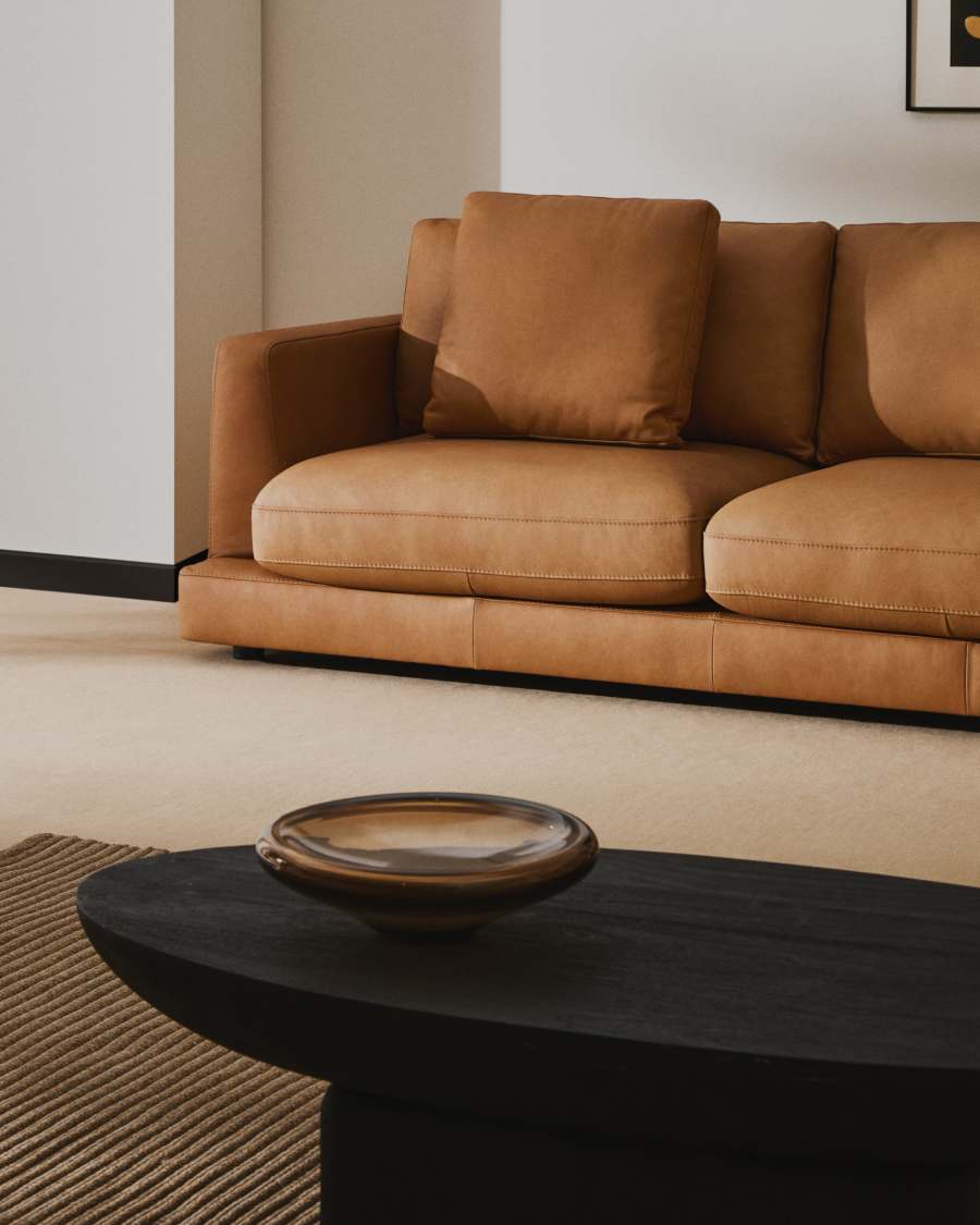 Gros plan de l'accoudoir et de l'assise du canapé Gala en cuir marron, table basse noire au premier plan.